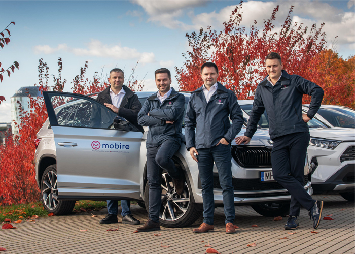 Four men in Mobire jackets standing next to a silver car with a Mobire logo, with red autumn trees in the background.